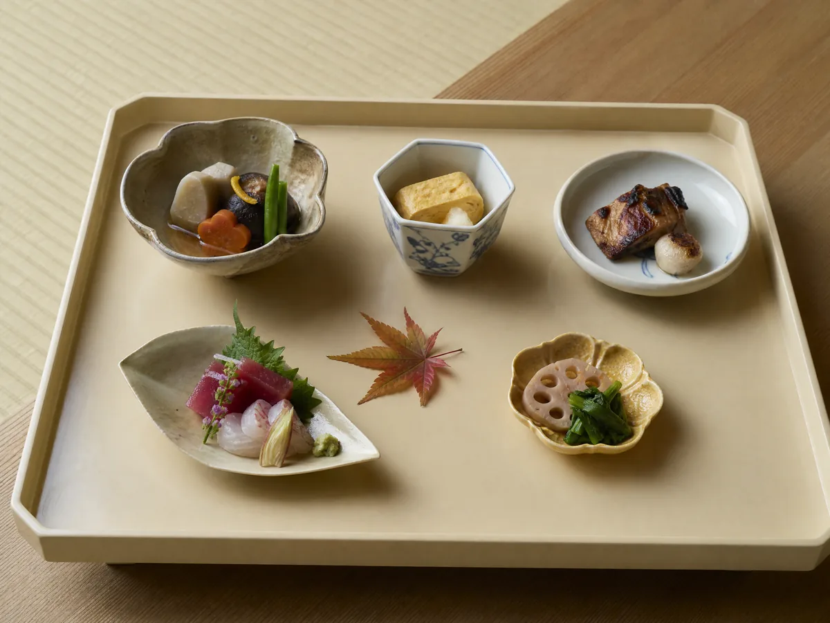 A kaiseki tray of small seasonal dishes in different ceramics, with sashimi, simmered vegetables and a maple leaf