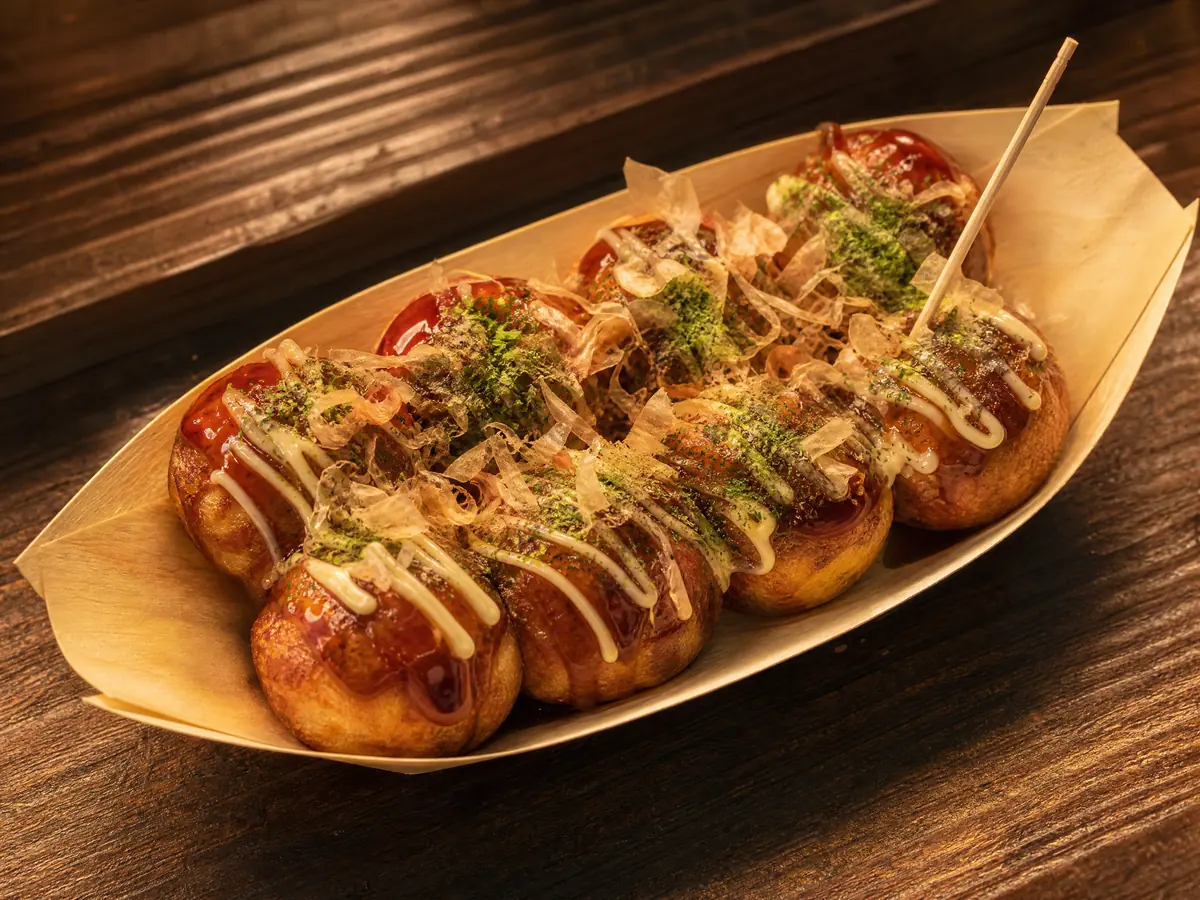 Takoyaki in a paper tray under brown sauce, mayonnaise, aonori and bonito flakes