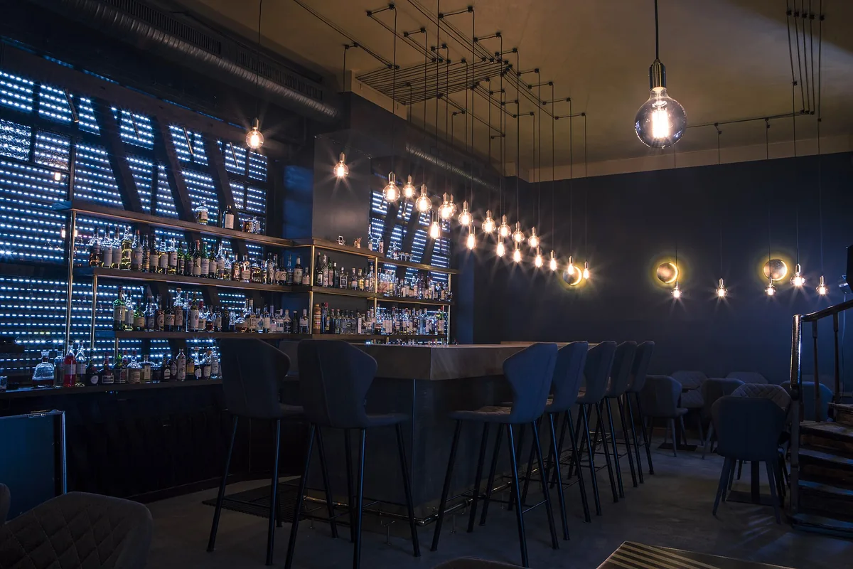 A dimly lit cocktail bar counter with a bartender stirring a drink