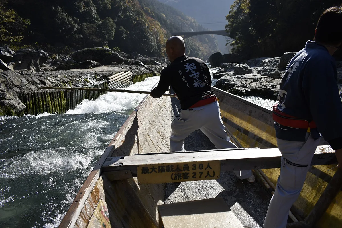 A flat-bottomed wooden boat being poled through the rapids of the Hozu gorge