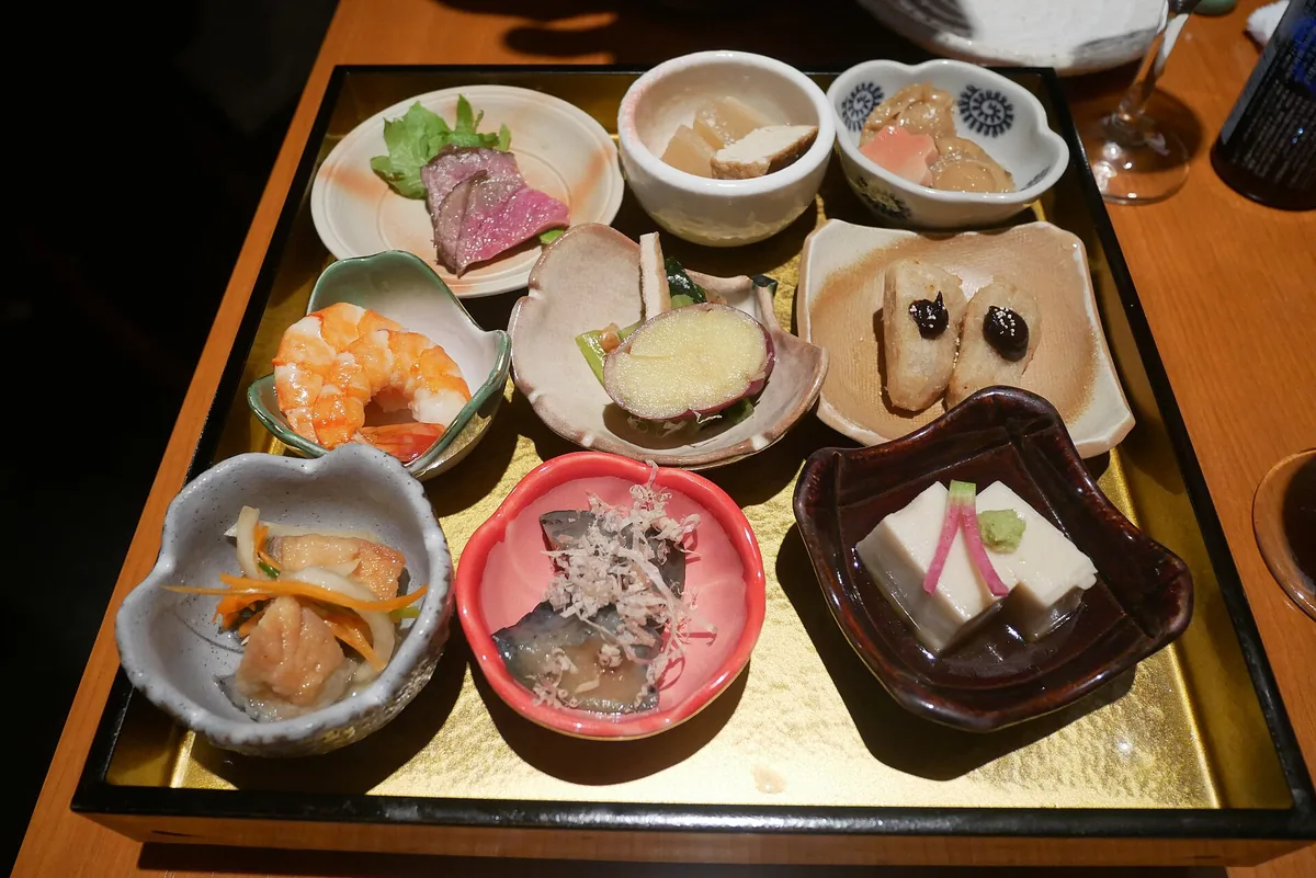 An array of small obanzai dishes in bowls along a restaurant counter