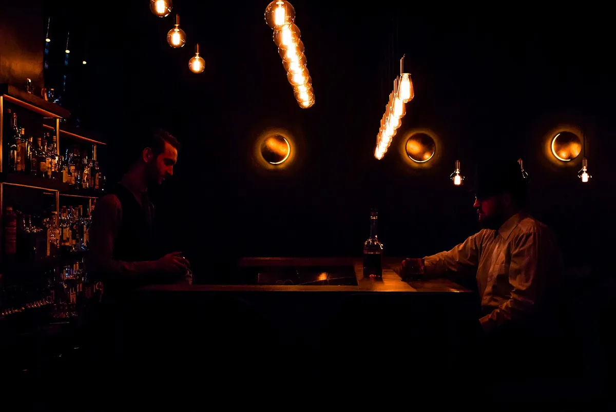 A bartender grinding herbs with a pestle and mortar behind a dark bar counter