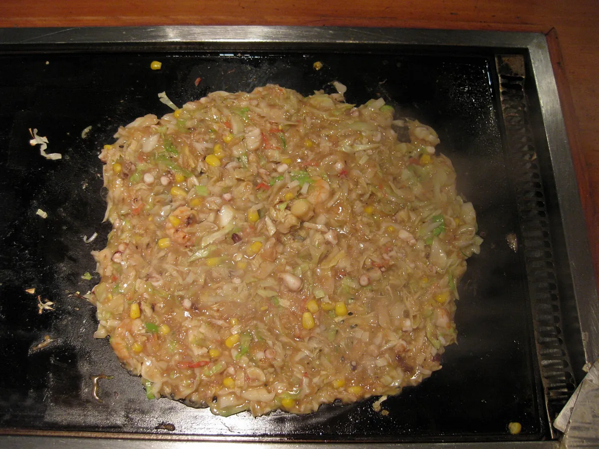 Monjayaki batter cooking on a hotplate with small metal spatulas