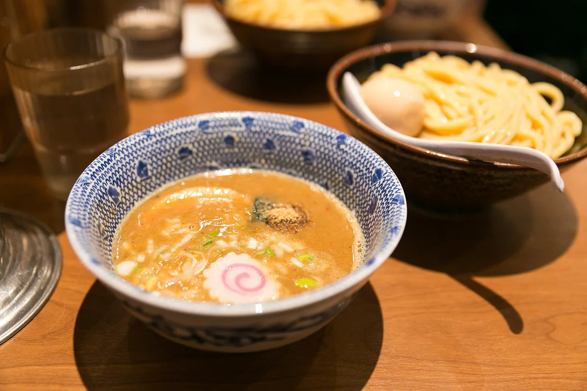 Thick tsukemen noodles beside a bowl of dark dipping broth